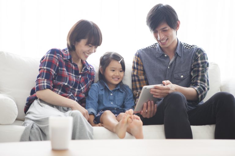 Parents and daughter are sitting on the sofa and using a digital tablet together.