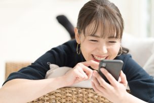 寝ころびながらスマートフォンを操作する女性